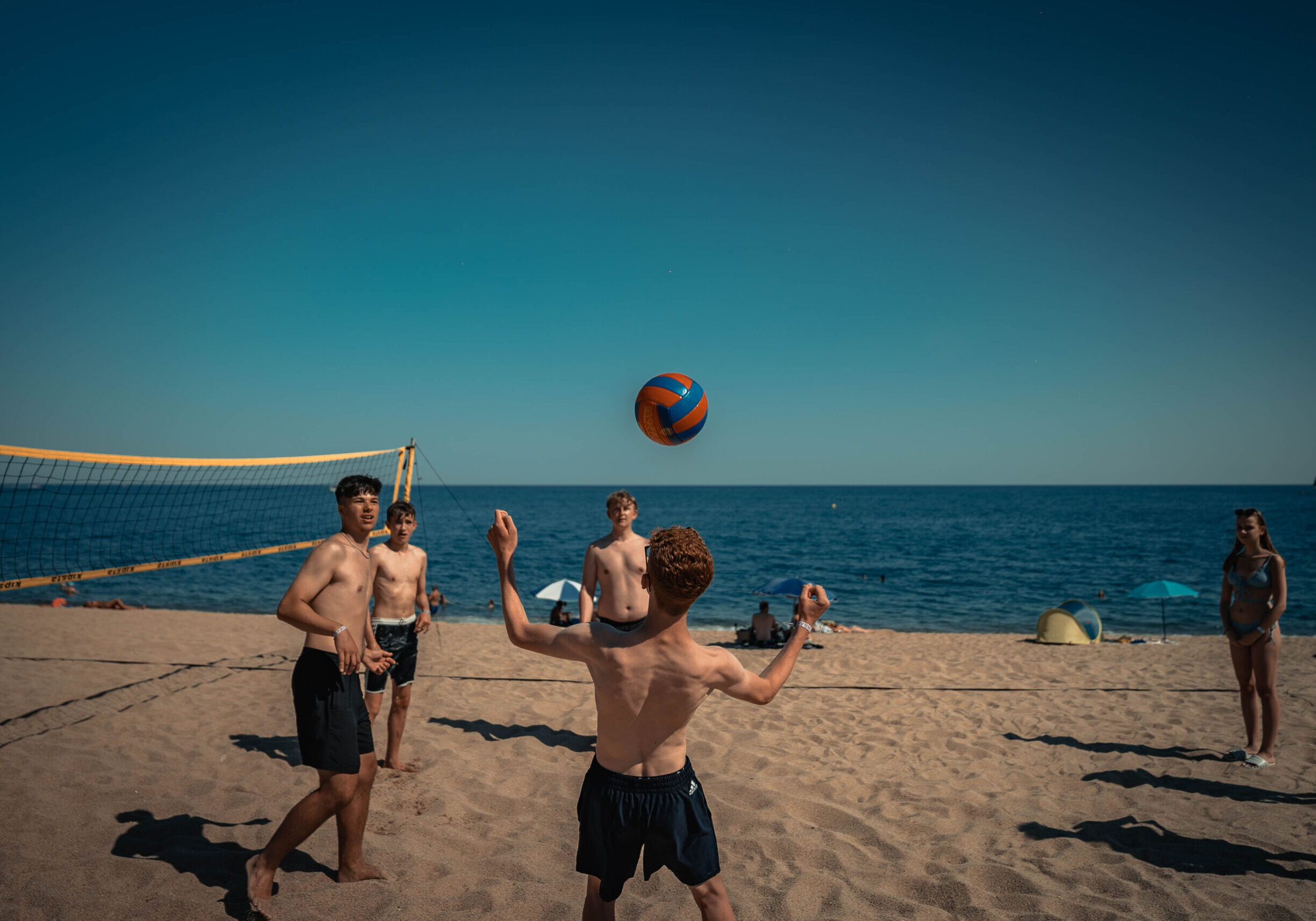 Vier junge Männer spielen Beachvolleyball an einem sonnigen Tag am Strand, einer bereitet sich darauf vor, den Ball anzunehmen