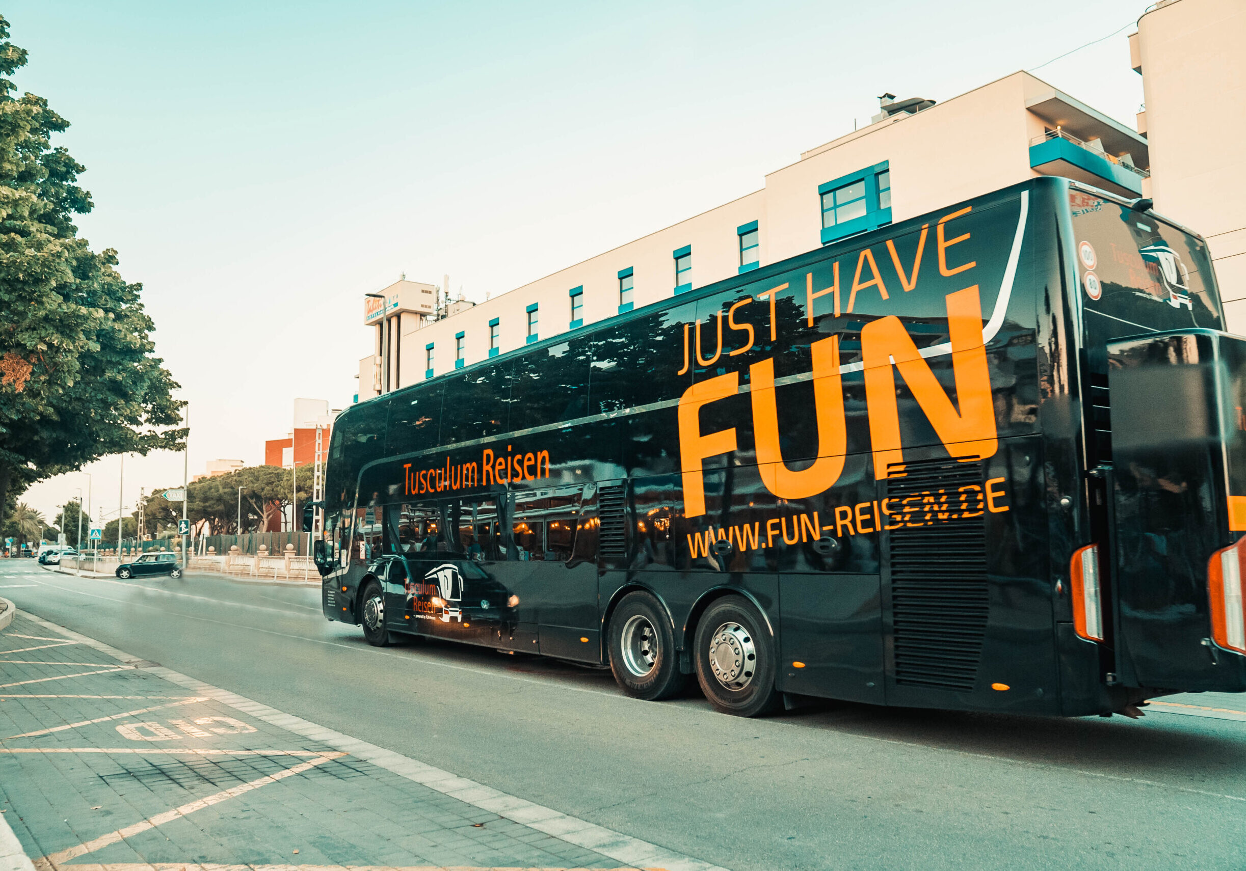 Ein moderner, schwarzer Reisebus von "FUN-REISEN.DE" mit dem großen orangefarbenen Slogan "JUST HAVE FUN" fährt auf einer Straße, bereit, junge Reisende zu ihren unvergesslichen Jugendreisezielen zu bringen.