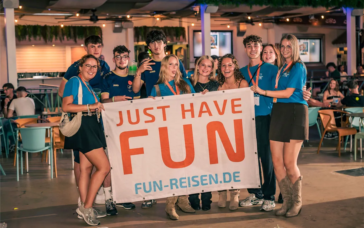Eine Gruppe Jugendlicher und Teamer hält lächelnd ein FUN-Reisen-Banner in die Kamera auf einer FUN-Jugendreise 2026.