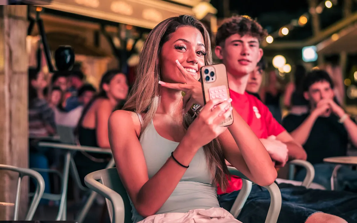Eine junge Frau macht lächelnd ein Selfie mit dem Peace-Zeichen in einer gemütlichen Outdoor-Bar auf einer FUN-Jugendreise 2026.