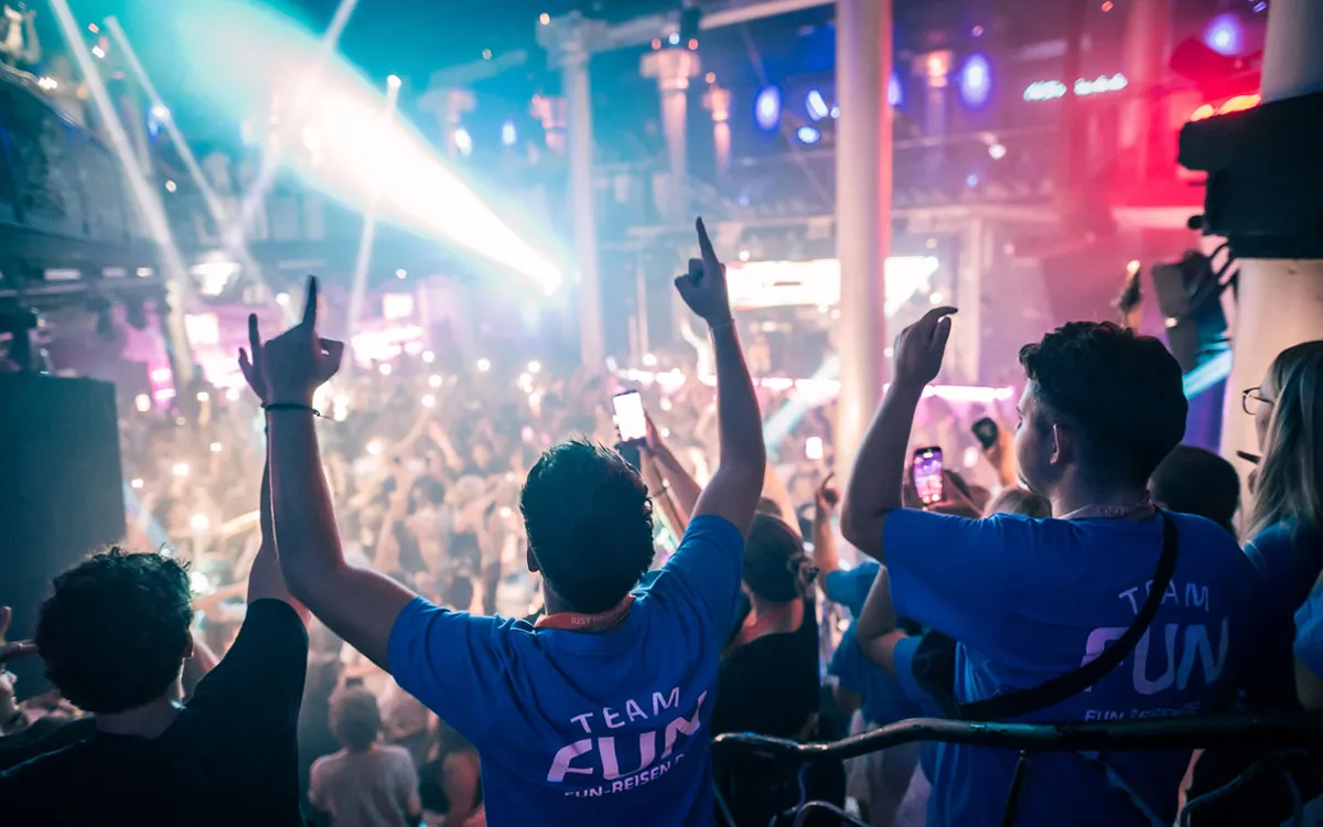 Zwei Teamer in blauen Shirts feiern mit erhobenen Händen in einem vollen Club auf einer FUN-Jugendreise 2026.