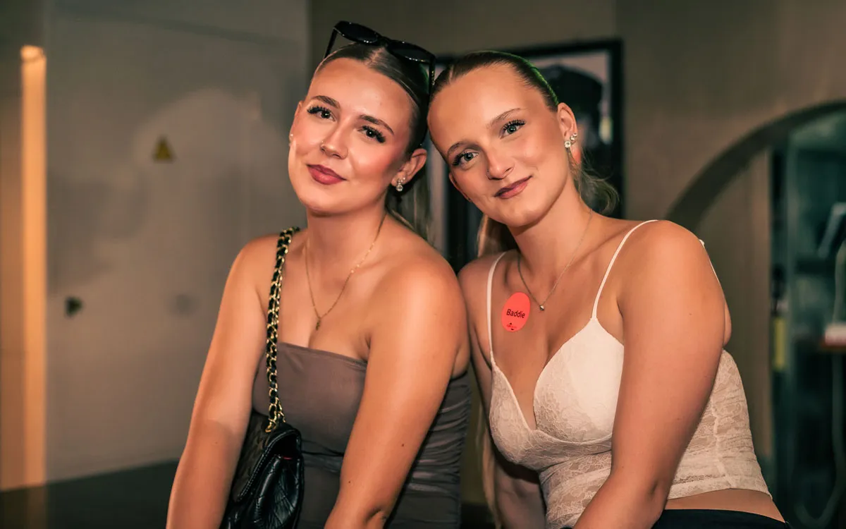 Zwei junge Frauen posieren lächelnd in schicken Partyoutfits vor dem Ausgehen auf einer FUN-Jugendreise 2026.