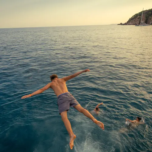 Junger Mann badet vom Katamaran aus in Malgrat de Mar und springt ins Wasser.