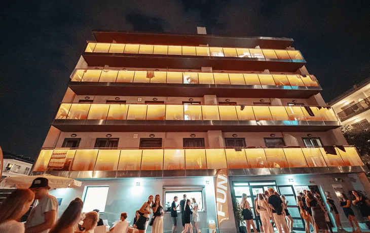 Ansicht des Hotels bei Nacht. Die Glasfronten der Balkone sind orange beleuchtet.