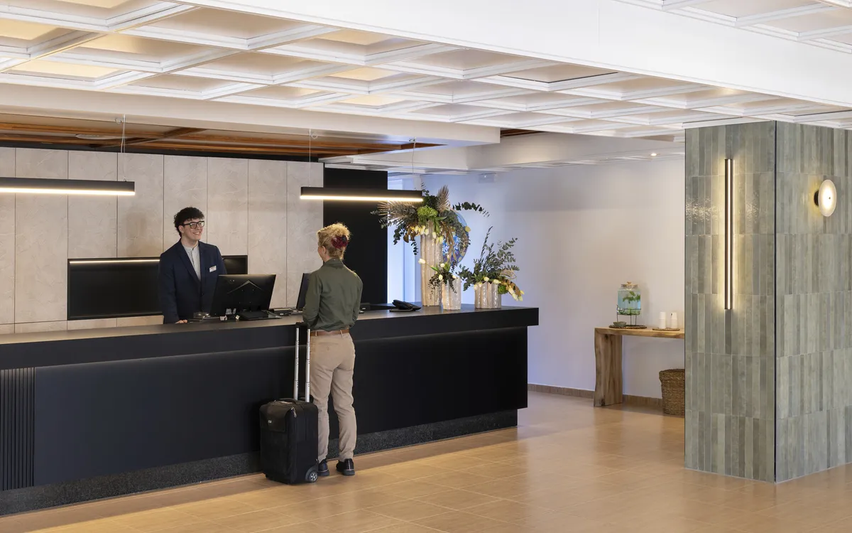 Rezeption eines Hotels mit Mitarbeiter und Gast mit Gepäck.