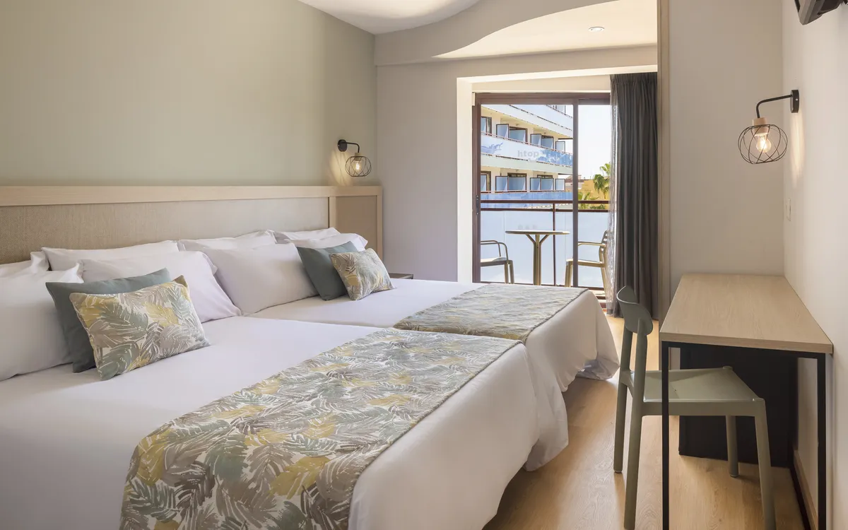 Hotelzimmer mit zwei Einzelbetten, Schreibtisch und Balkonblick.