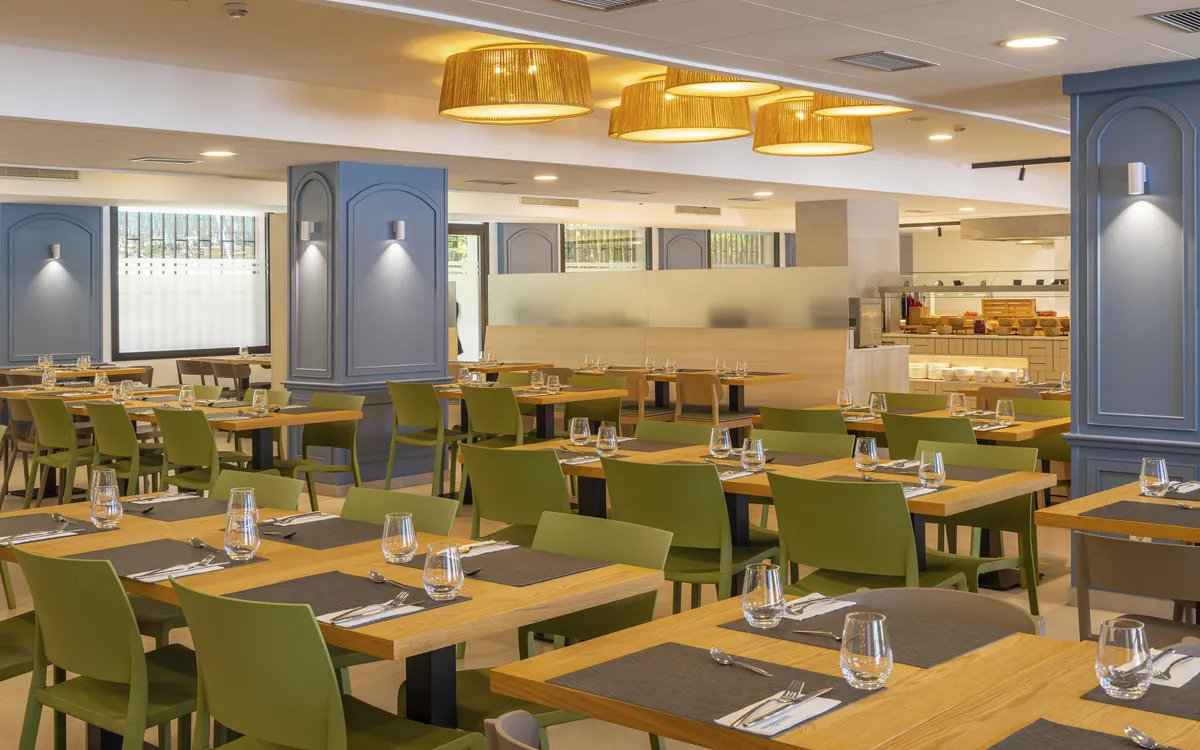 Geräumiger, moderner Speisesaal mit gedeckten Holztischen, grünen Stühlen und Buffetbereich.