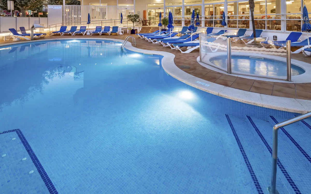 Ein blauer Swimmingpool im ruhigen Innenhof des Hotels, umgeben von Sonnenliegen und Palmen.