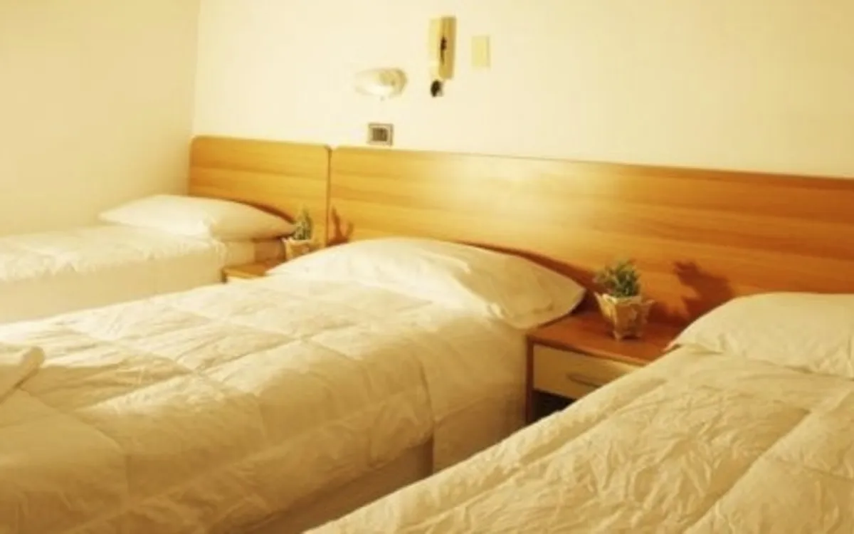 Dreibettzimmer in einem Hotel mit drei Einzelbetten, weisser Bettwäsche und Handtüchern.