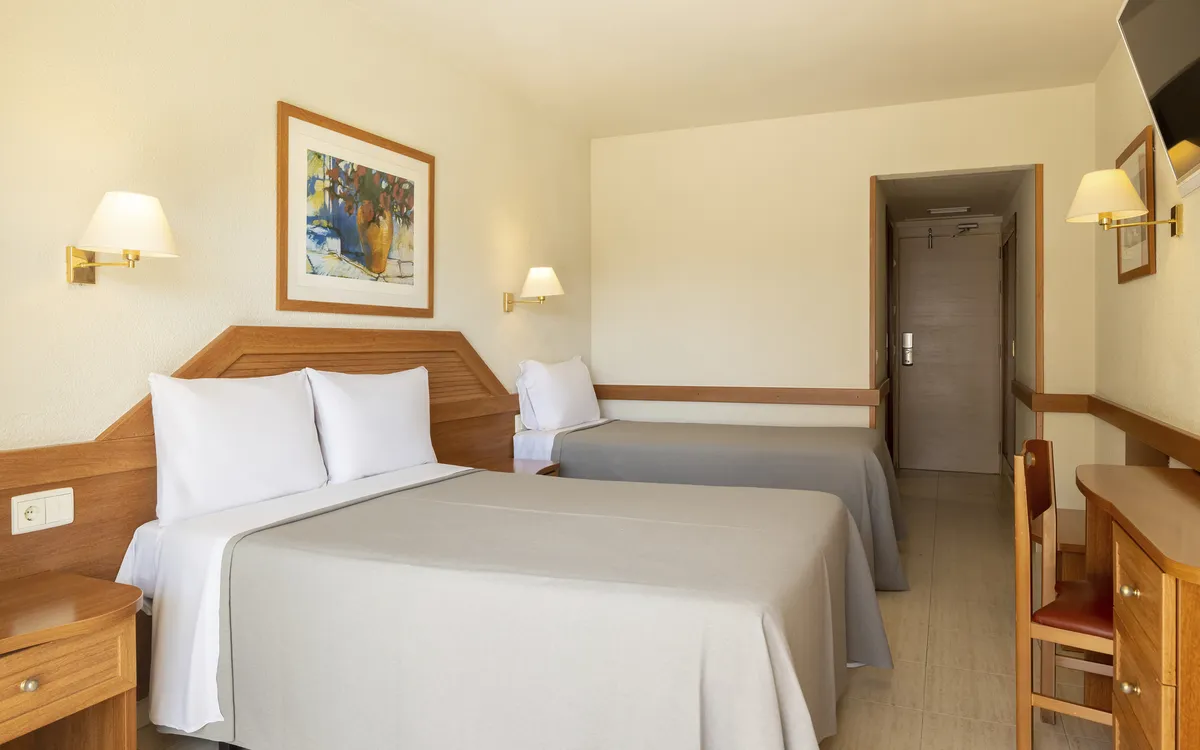 Ein helles, klimatisiertes Hotelzimmer mit zwei Einzelbetten, Schreibtisch, TV und Zugang zu einem privaten Balkon.
